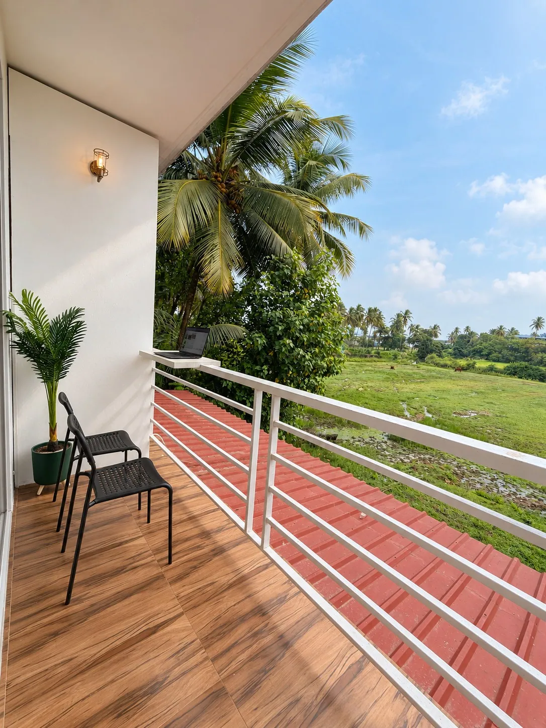 The balcony with a chair and a plant, and palms and greenery beyond the railing