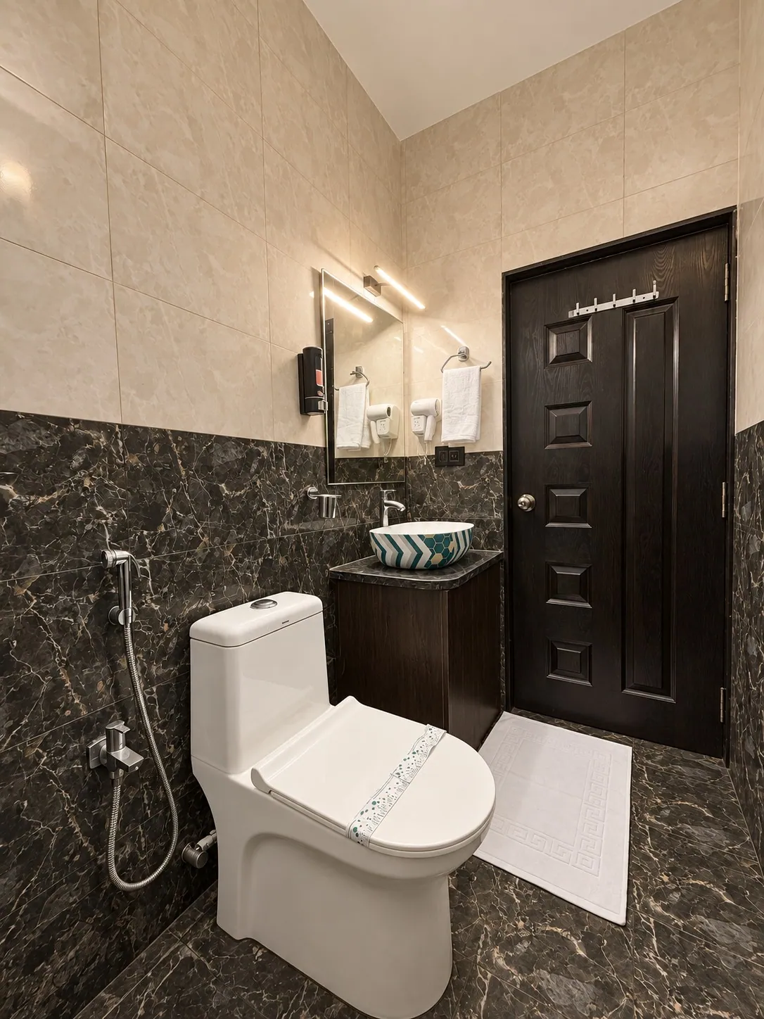 The full bathroom, with dark marble-look tiles and a white bath mat
