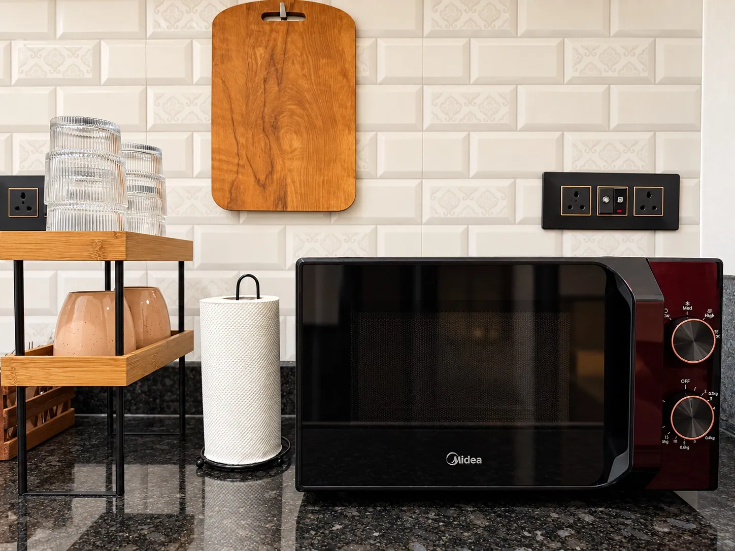 The microwave on the granite counter, with mugs and a wooden chopping board