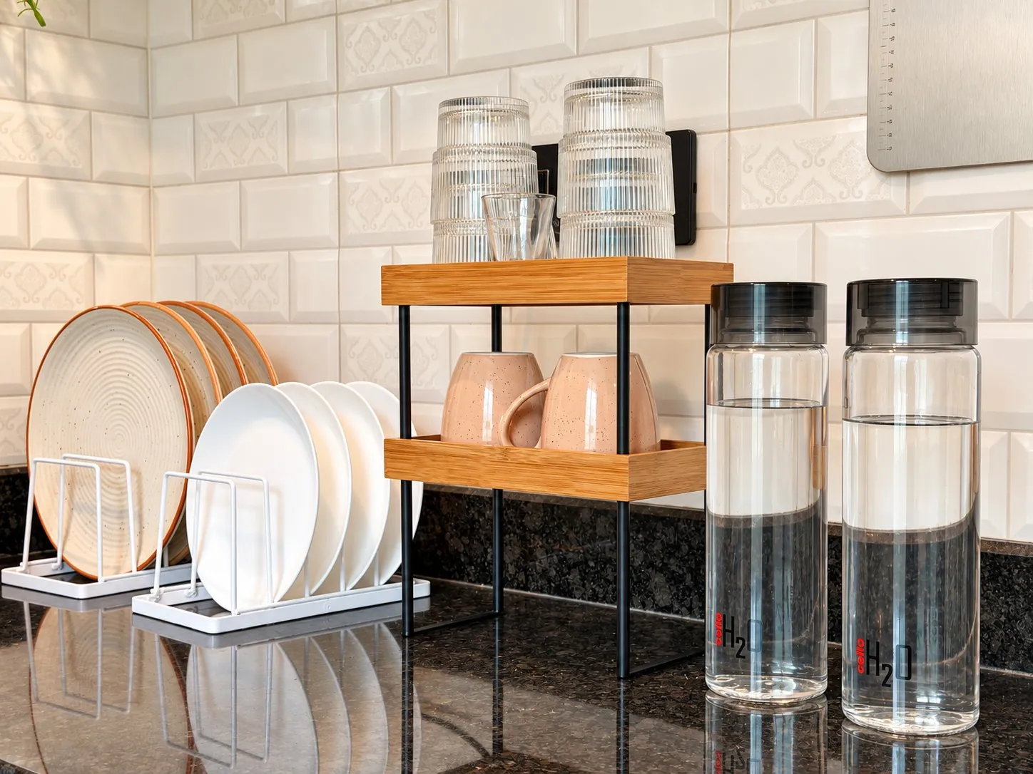Plates in a rack, mugs and water bottles against the white tiles